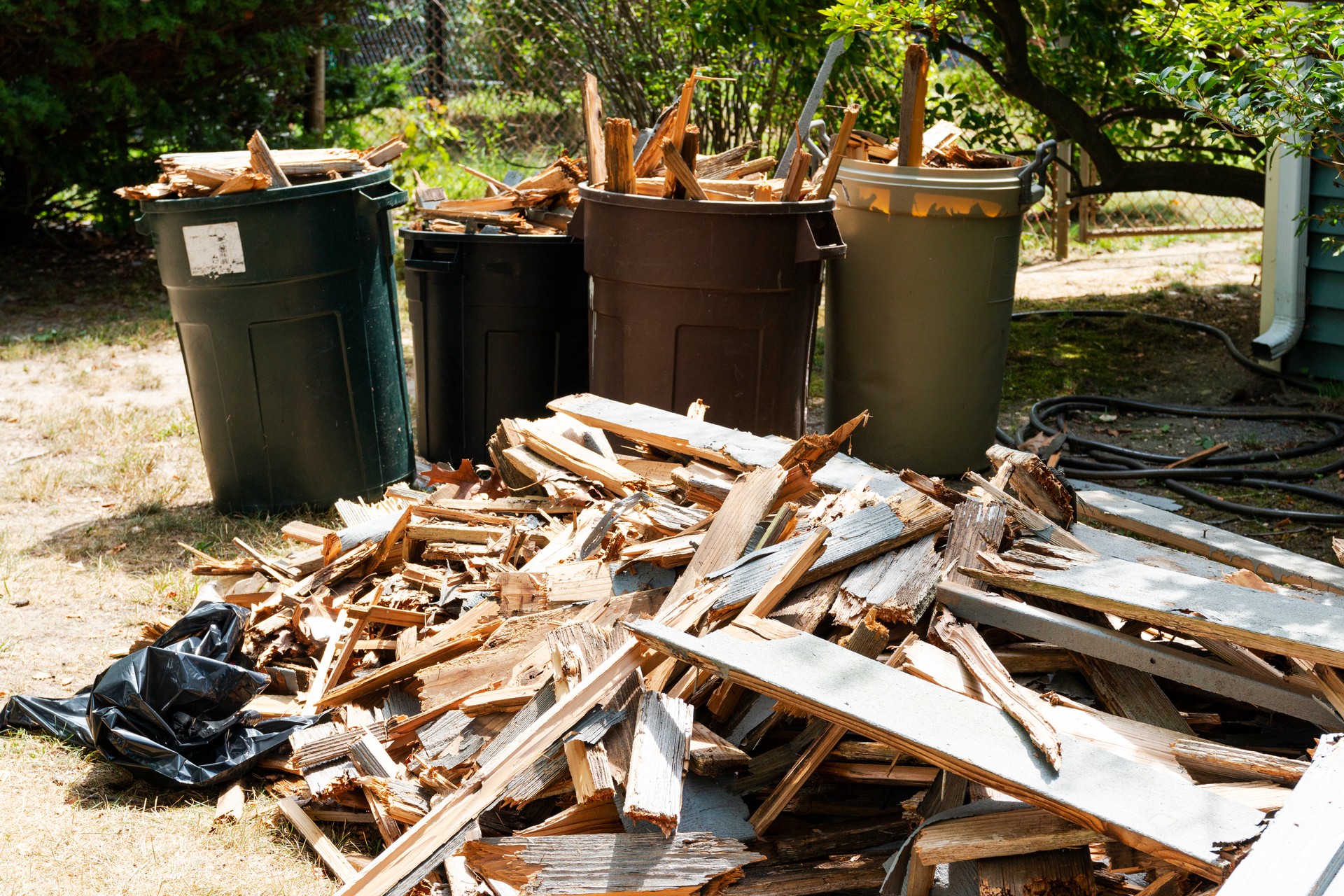 Rotted wood from a deck piled up on the ground next to garbage pales